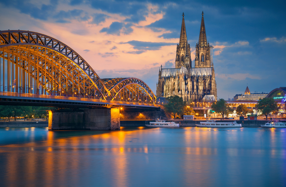 Catedral de Colonia y el puente Hohenzollern iluminados al anochecer, reflejados en el río Rin, Alemania